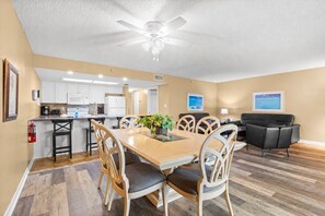 A spacious living area with a dining table, chairs, a black leather sofa, and a ceiling fan.