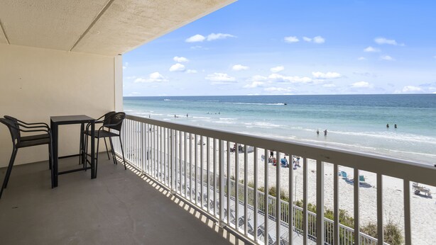 Een balkon met uitzicht op het strand, een tafel en twee stoelen.