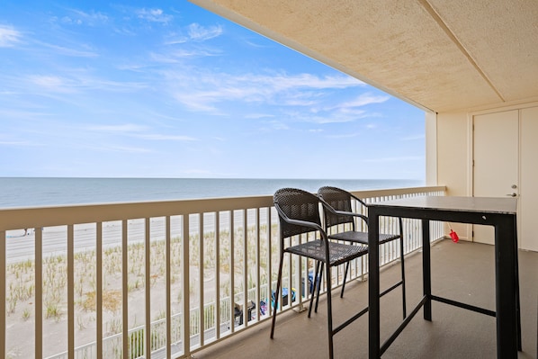 A balcony with a view of the beach, two wicker chairs, and a table.