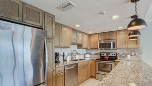 Uma cozinha moderna com eletrodomésticos de aço inoxidável, armários de madeira, bancadas de granito e iluminação pendente.