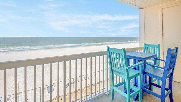 Un balcon avec vue sur la plage, une table et deux chaises.