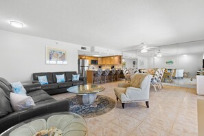 A modern living room with a sofa, armchairs, a coffee table, and a kitchen in the background. - Panoramic Gulf Views – Spacious 2BR Condo at Fifty Gulfside Unit #316  2BR/2BA  Sleeps 6 (Indian Rocks Beach)