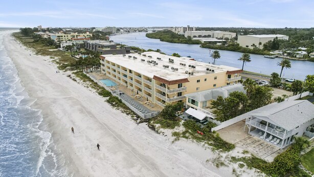 Ett hotell vid stranden med flera balkonger, en pool och utsikt över stranden och floden.