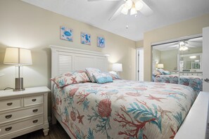 A bedroom with a bed, nightstands, a dresser, a ceiling fan, and wall art.
