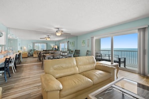 A spacious living area with a leather sofa, dining table, chairs, and a balcony with a view of the ocean.