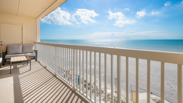 Ein Balkon mit Blick auf den Strand, einer Couch und einem Tisch.