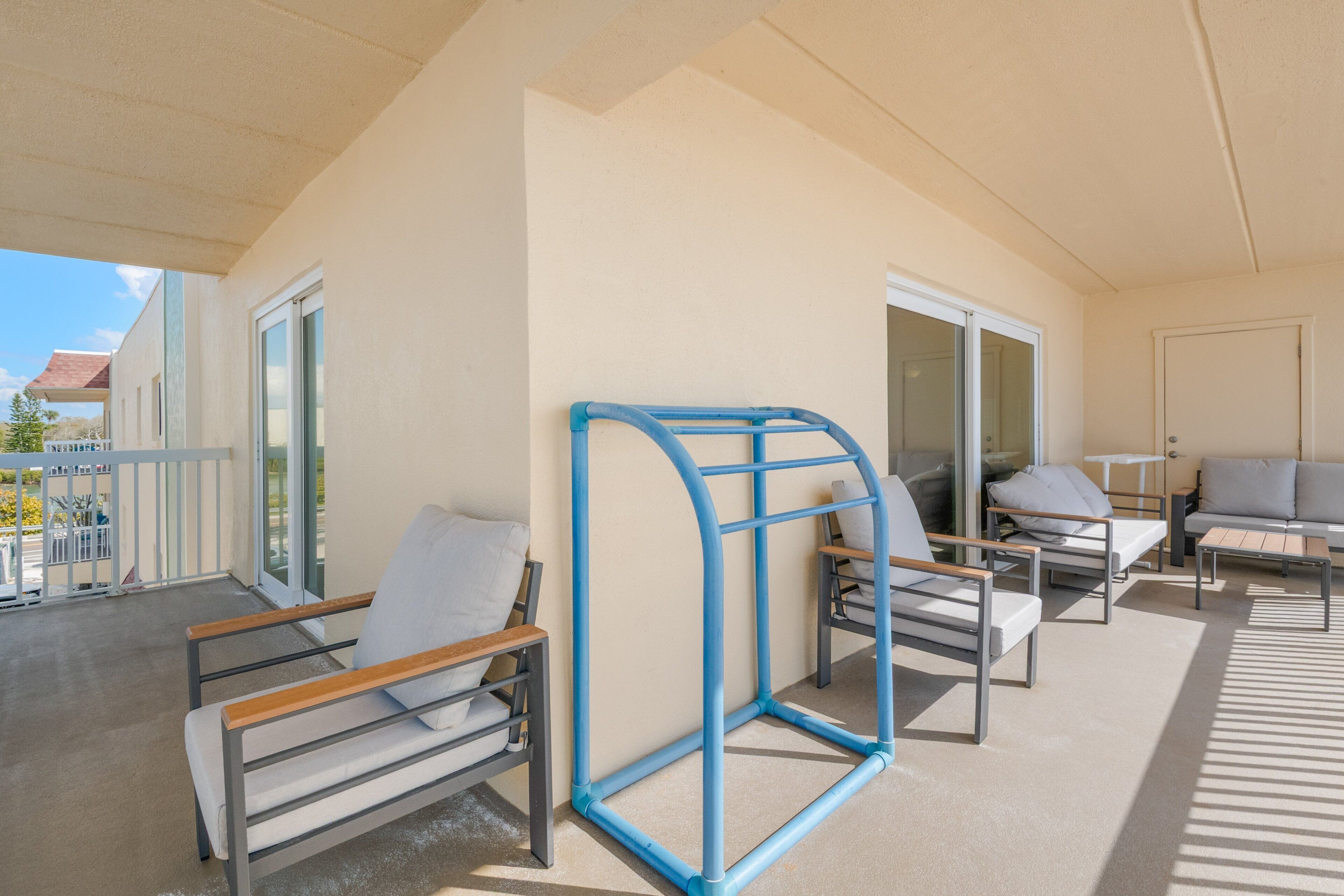 Ein Balkon mit Sitzgelegenheiten im Freien, darunter eine Couch und Stühle, sowie eine blaue Metallkonstruktion.
