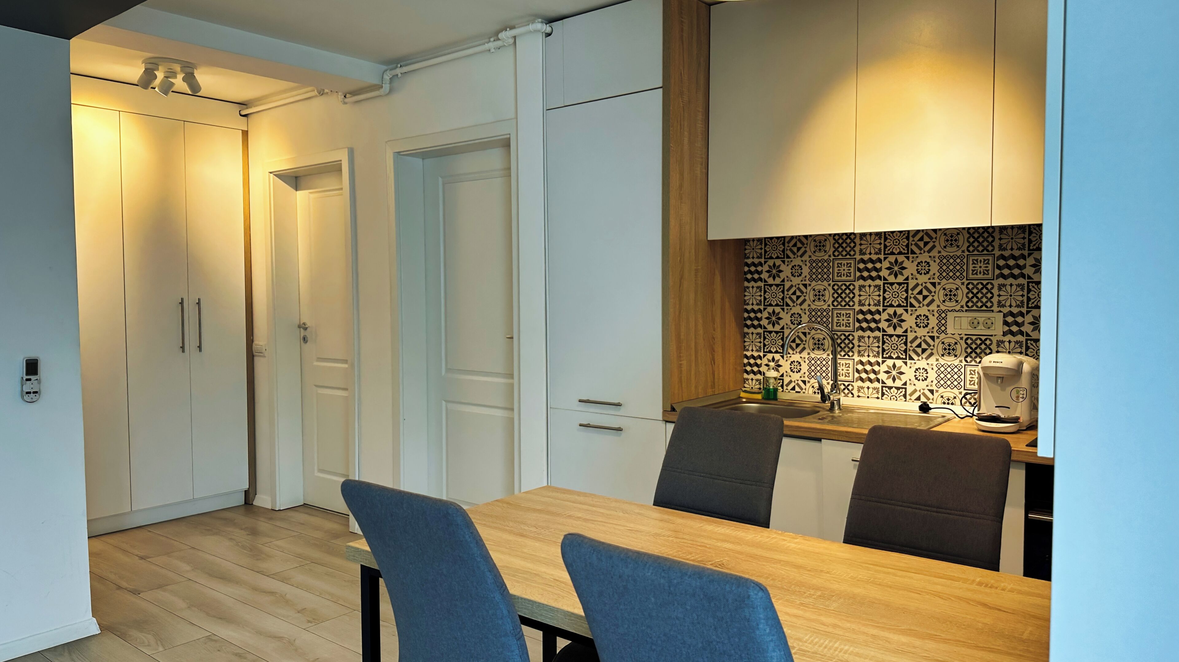Une cuisine moderne avec des meubles blancs, une table à manger en bois et un crédence décorée de motifs.