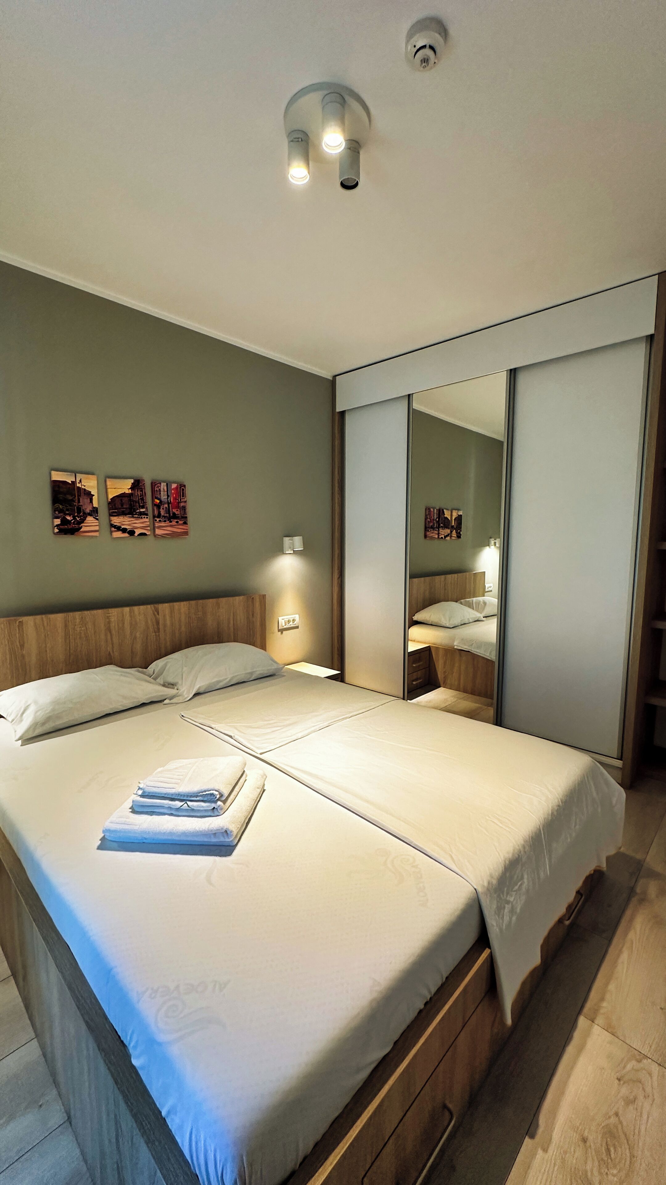 Un dormitorio moderno con una cama grande, mesitas de noche, un espejo y obras de arte en la pared.
