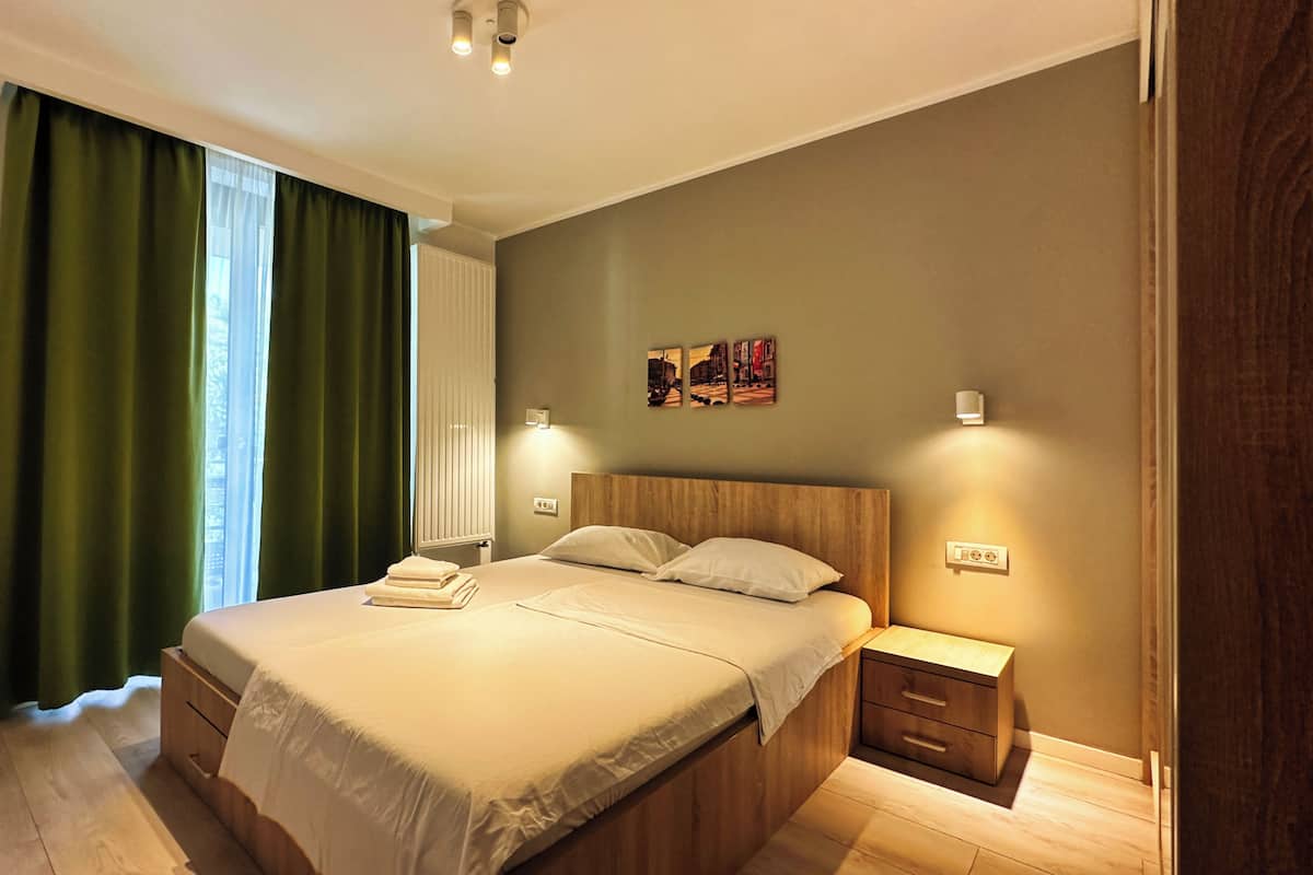 A modern bedroom with a large bed, bedside tables, and a window with green curtains.
