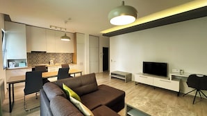 A modern living room with a sectional sofa, a flat-screen TV, a dining area with a table and chairs, and a kitchen with patterned backsplash and white cabinets. - Timisoara Prime Residence | powered by NEO (Timisoara)