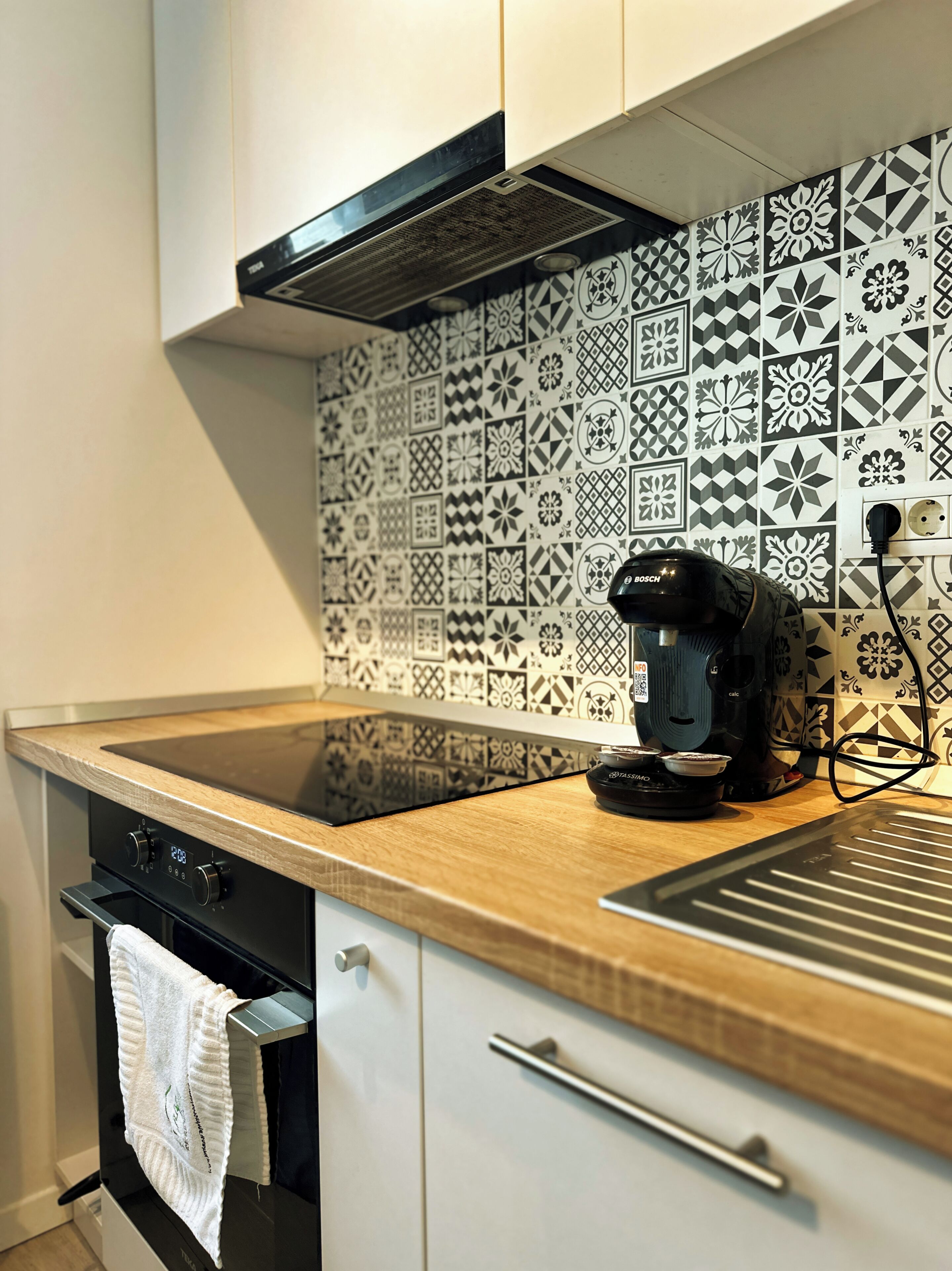 Una cocina con una cafetera Bosch negra sobre la encimera, un lavabo de acero inoxidable y un salpicadero decorado.