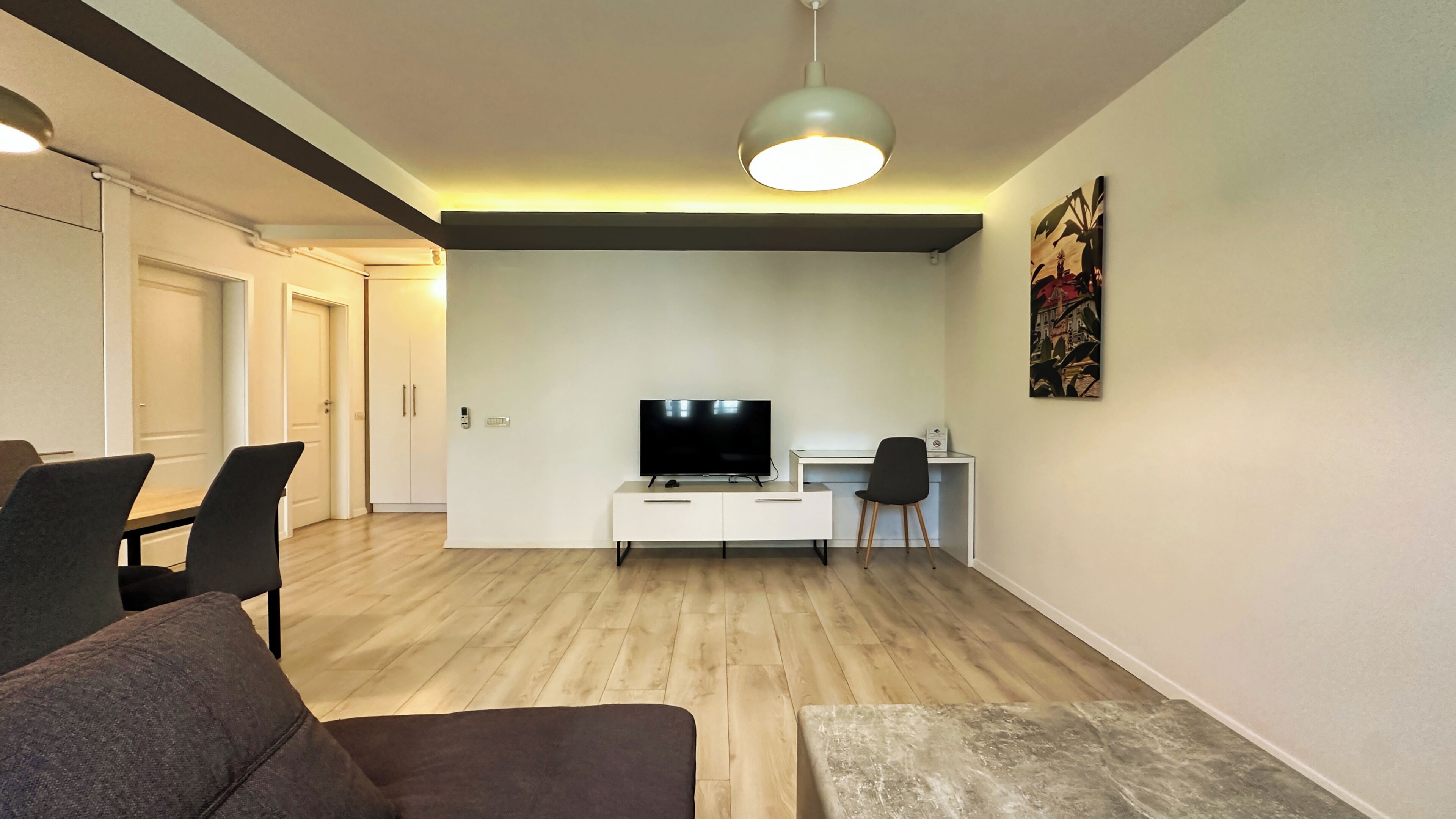 A modern living room with a flat-screen TV, a white cabinet, and a desk with a chair.