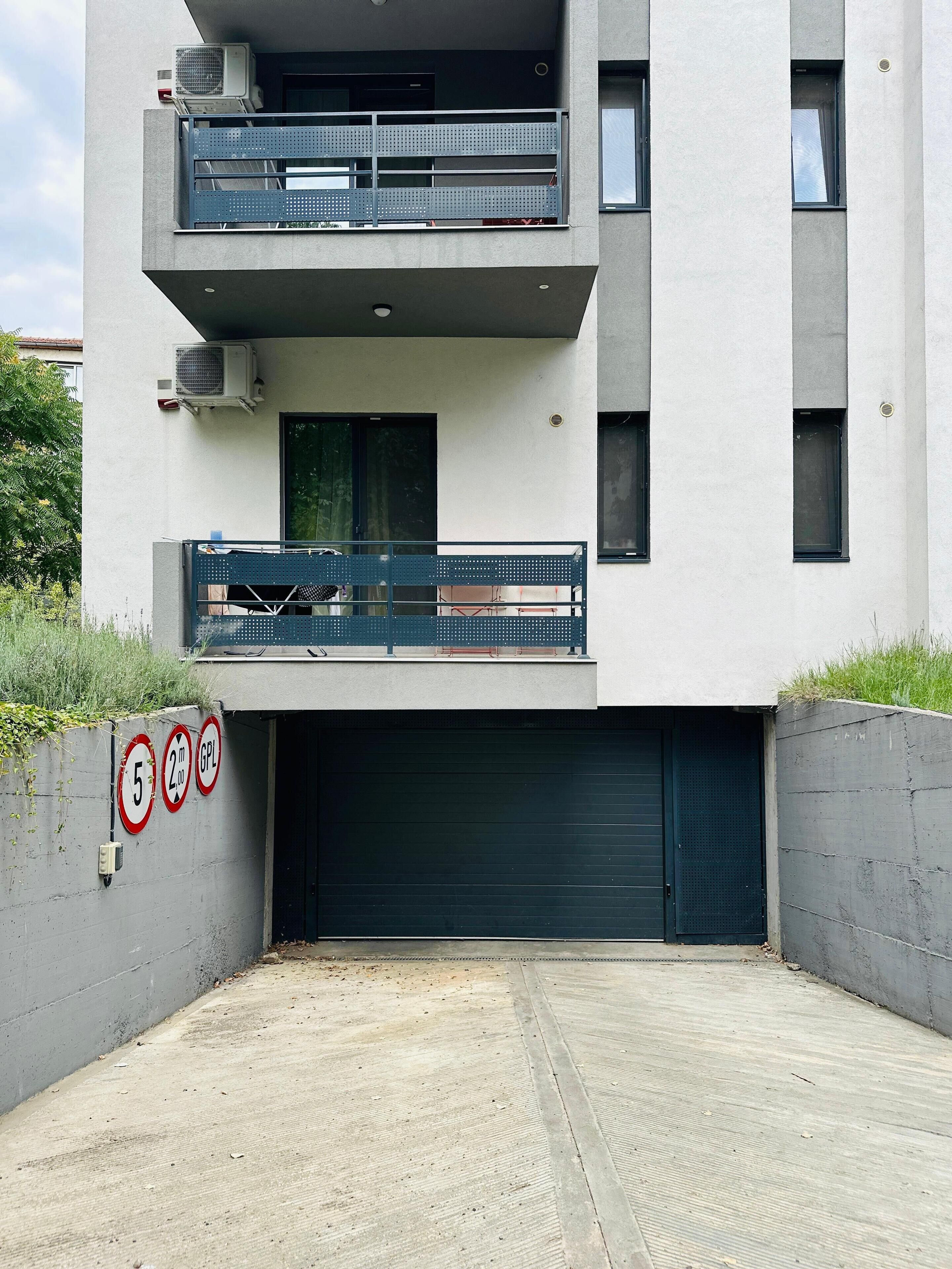 Un edificio moderno con una puerta de garaje doble, un balcón con barandilla metálica y un aire acondicionado instalado en la pared.