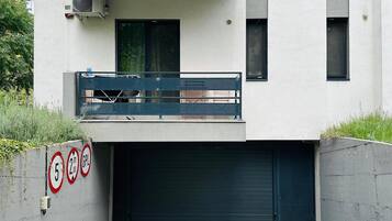 Un edificio moderno con una puerta de garaje doble, un balcón con barandilla metálica y un aire acondicionado instalado en la pared.