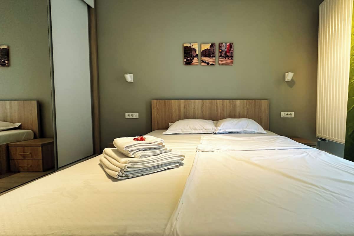 A neatly made bed with white linens, a stack of folded towels, and two wall-mounted light switches.