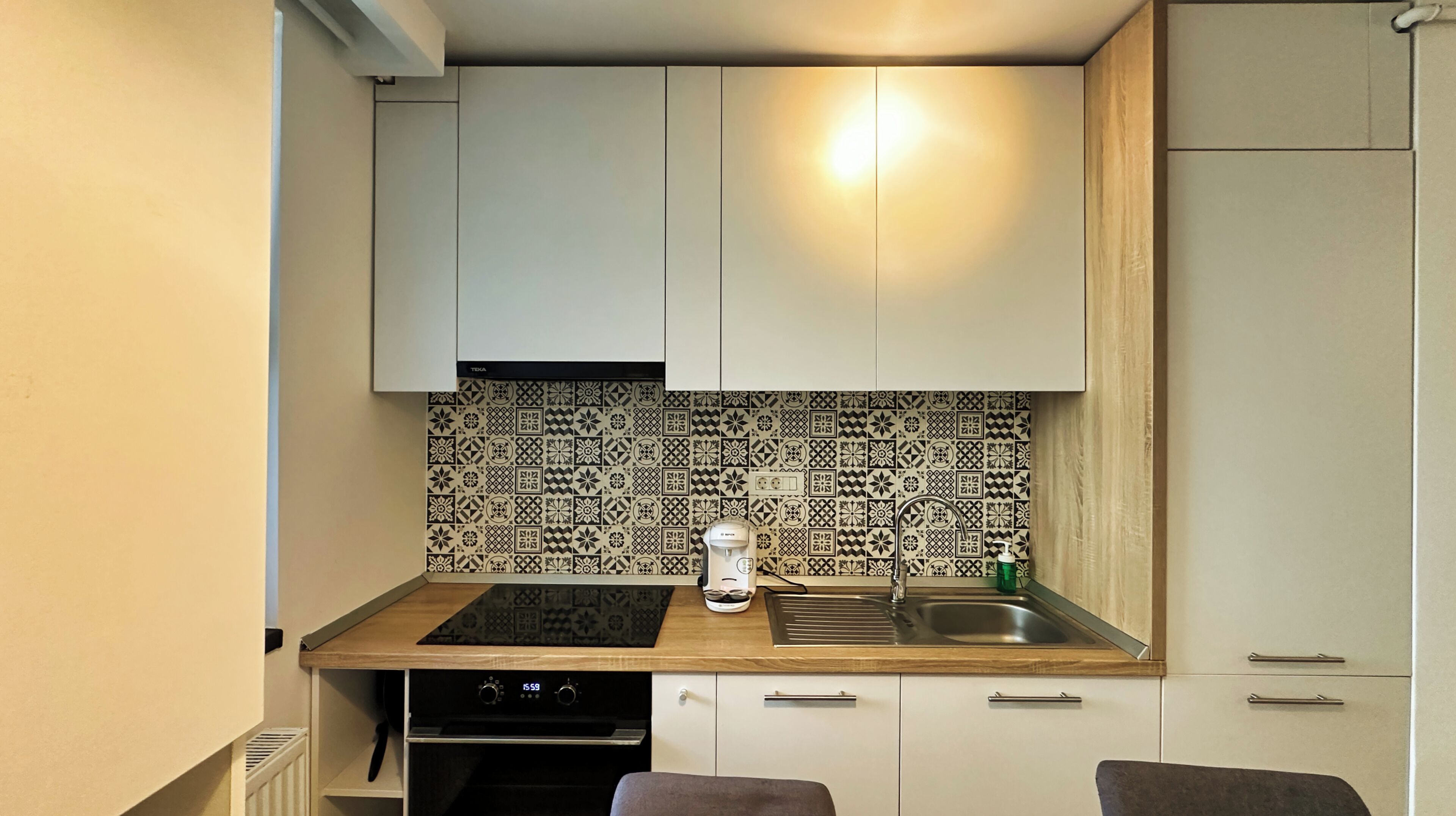 Una cocina compacta con armarios blancos, una encimera negra, una cafetera y un lavabo.