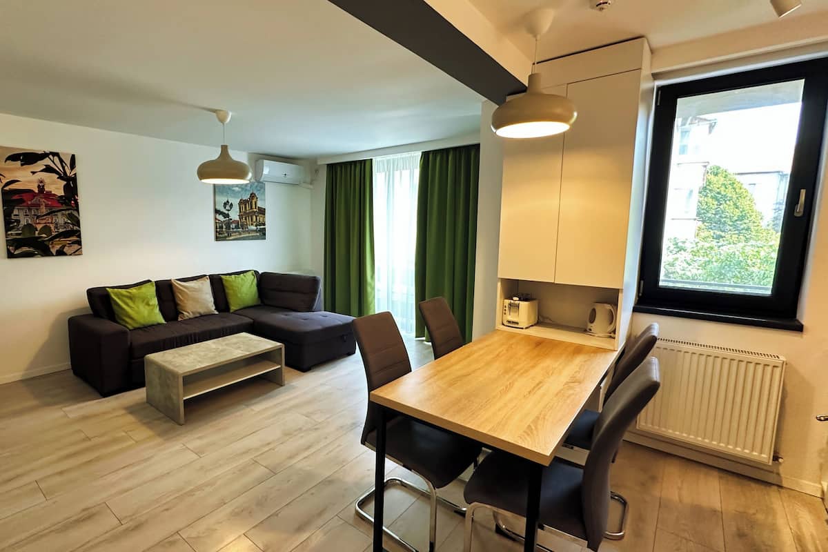 A modern living room with a sectional sofa, a wooden dining table, and a large window with curtains.