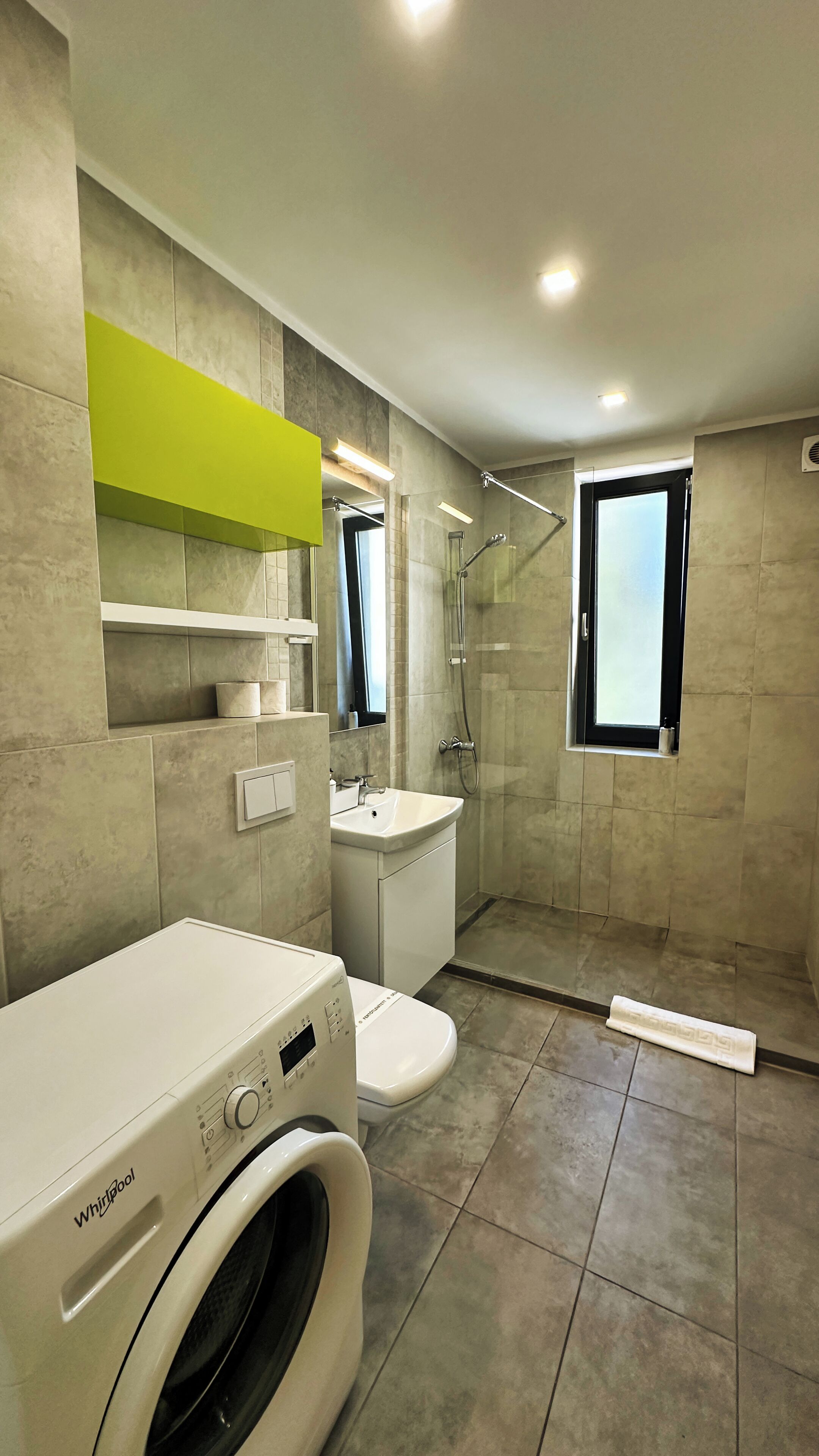 Un bagno moderno con lavatrice integrata, un water, una doccia e uno specchio grande.
