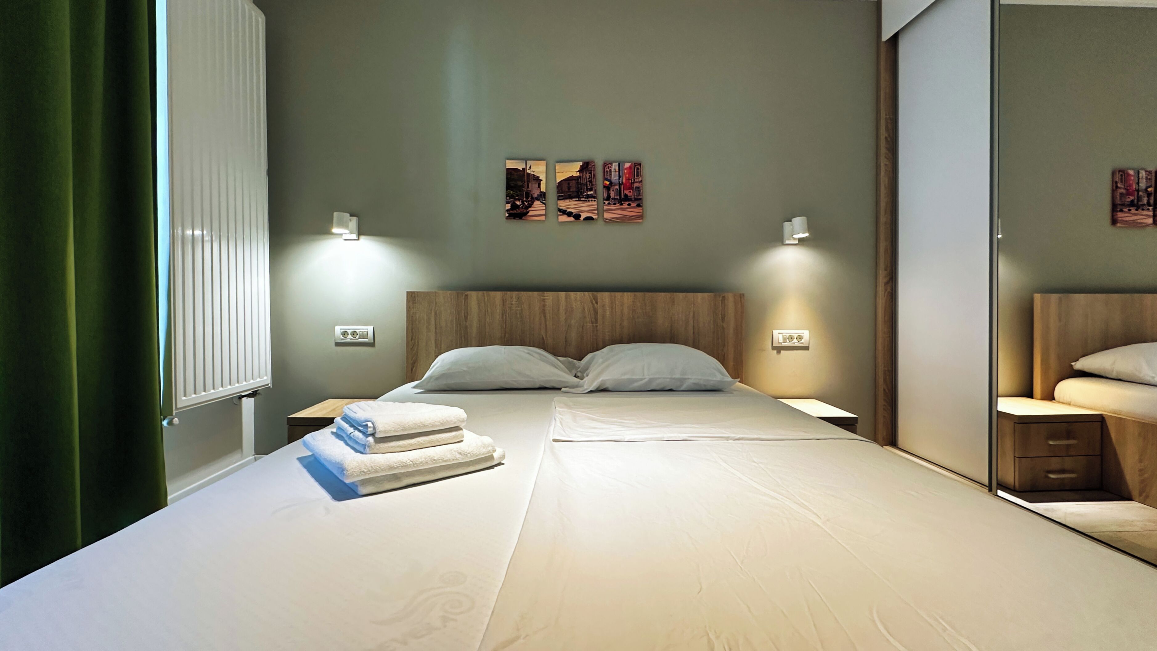 A modern hotel room with a large bed, two bedside tables, a mirror, and artwork on the wall.