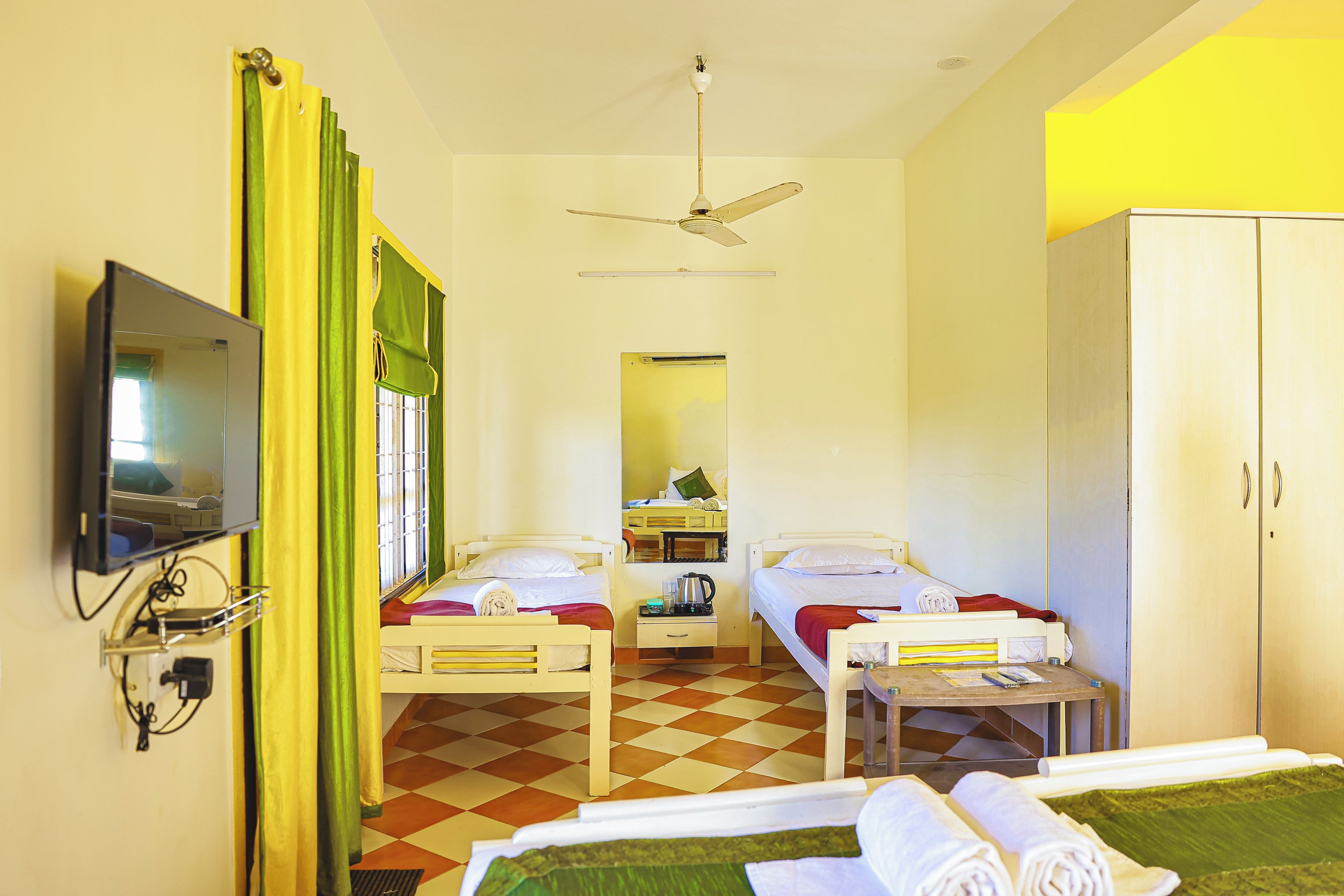 A hotel room with two beds, a television, a ceiling fan, and a wardrobe.