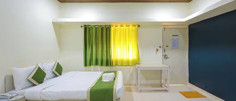 A hotel room with two beds, a small table, a curtain, and a door.
