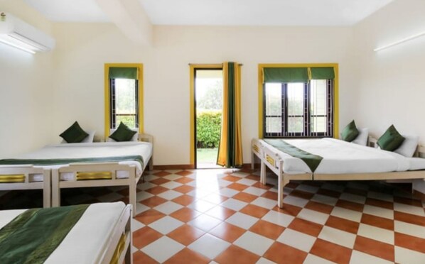 A room with two single beds, each with a green pillow and a white bedspread. There are two windows with yellow frames and green curtains. The floor has a checkered pattern.
