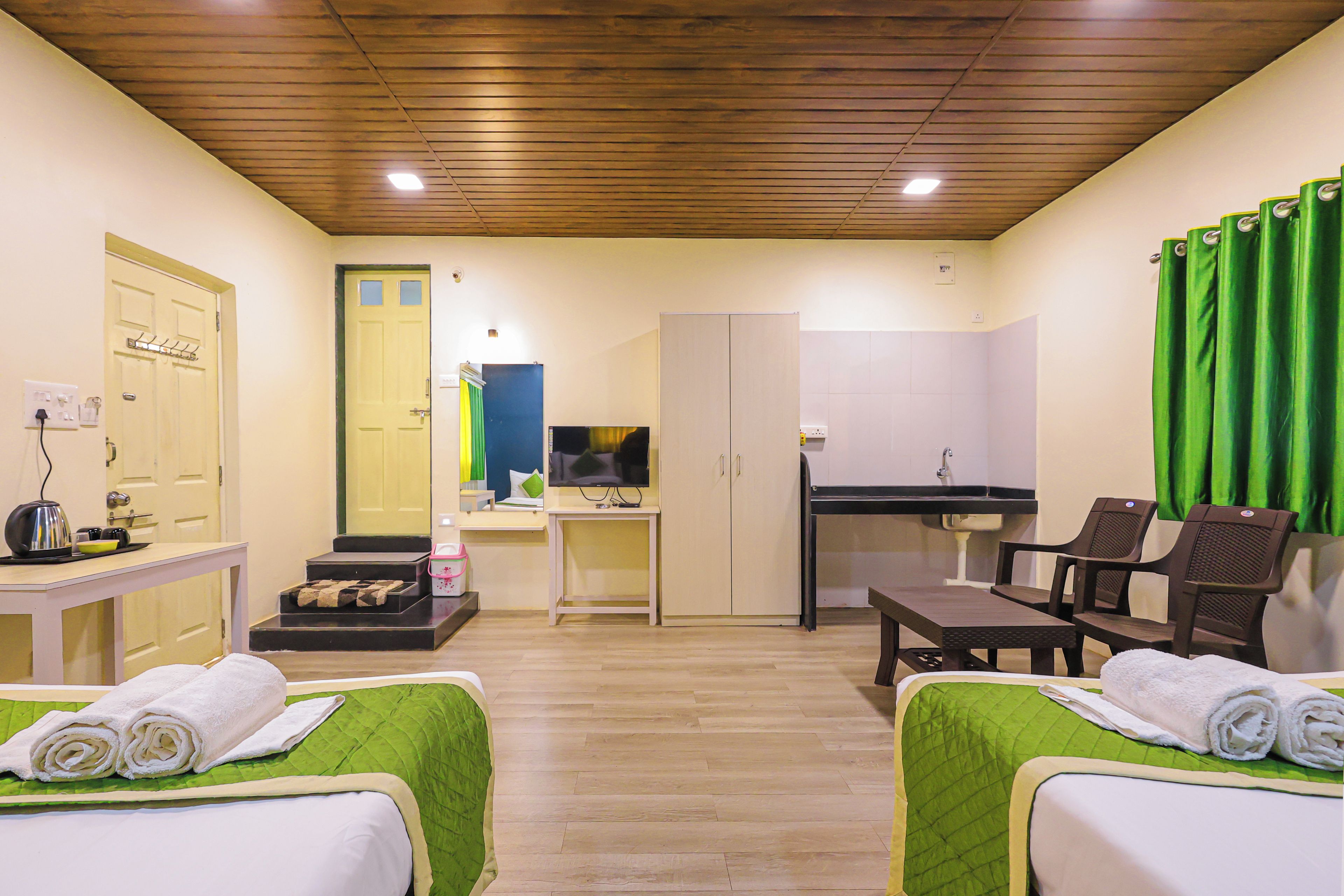 A hotel room with two beds, a desk, a chair, a small kitchenette, and a bathroom.