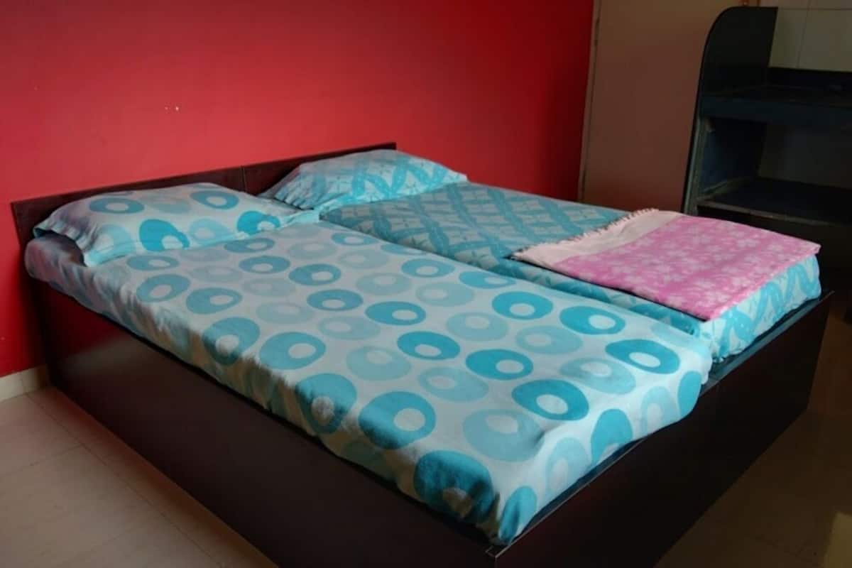 A bed with patterned bedding, a pink blanket, and a metal bunk bed in the background.