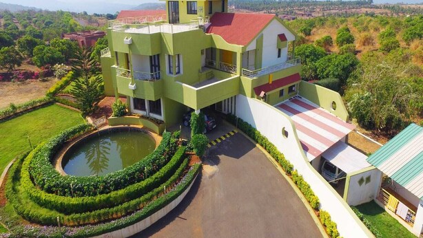A multi-story building with a central courtyard, a swimming pool, and a red-roofed annex. - Kokanwadi Resort (Ratnagiri)