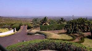 A landscaped area with a curved driveway, palm trees, and a view of distant hills. - Kokanwadi Resort (Ratnagiri)