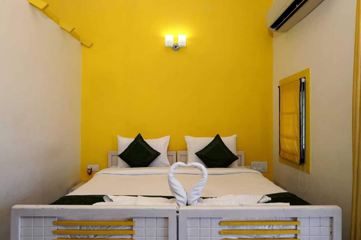 A bed with a heart-shaped towel in the middle, two pillows, and a wall-mounted light fixture.