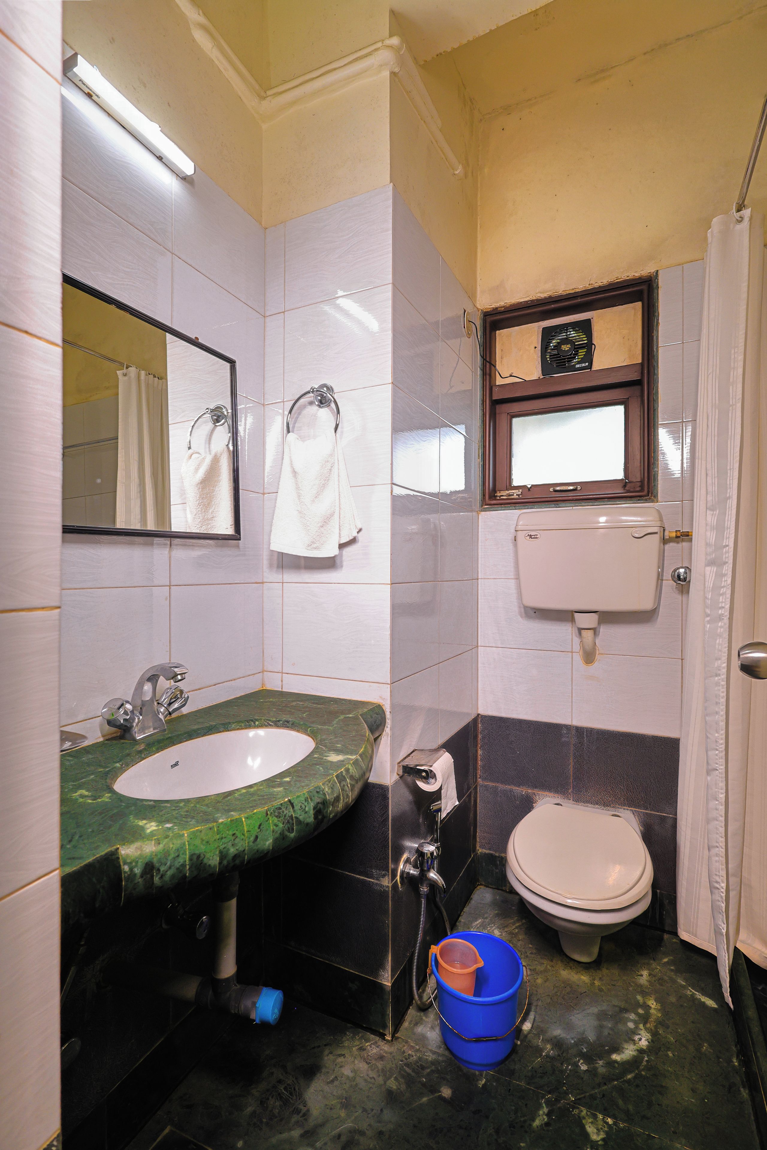 Een compacte badkamer met een wastafel, spiegel, toilet en een blauwe emmer.