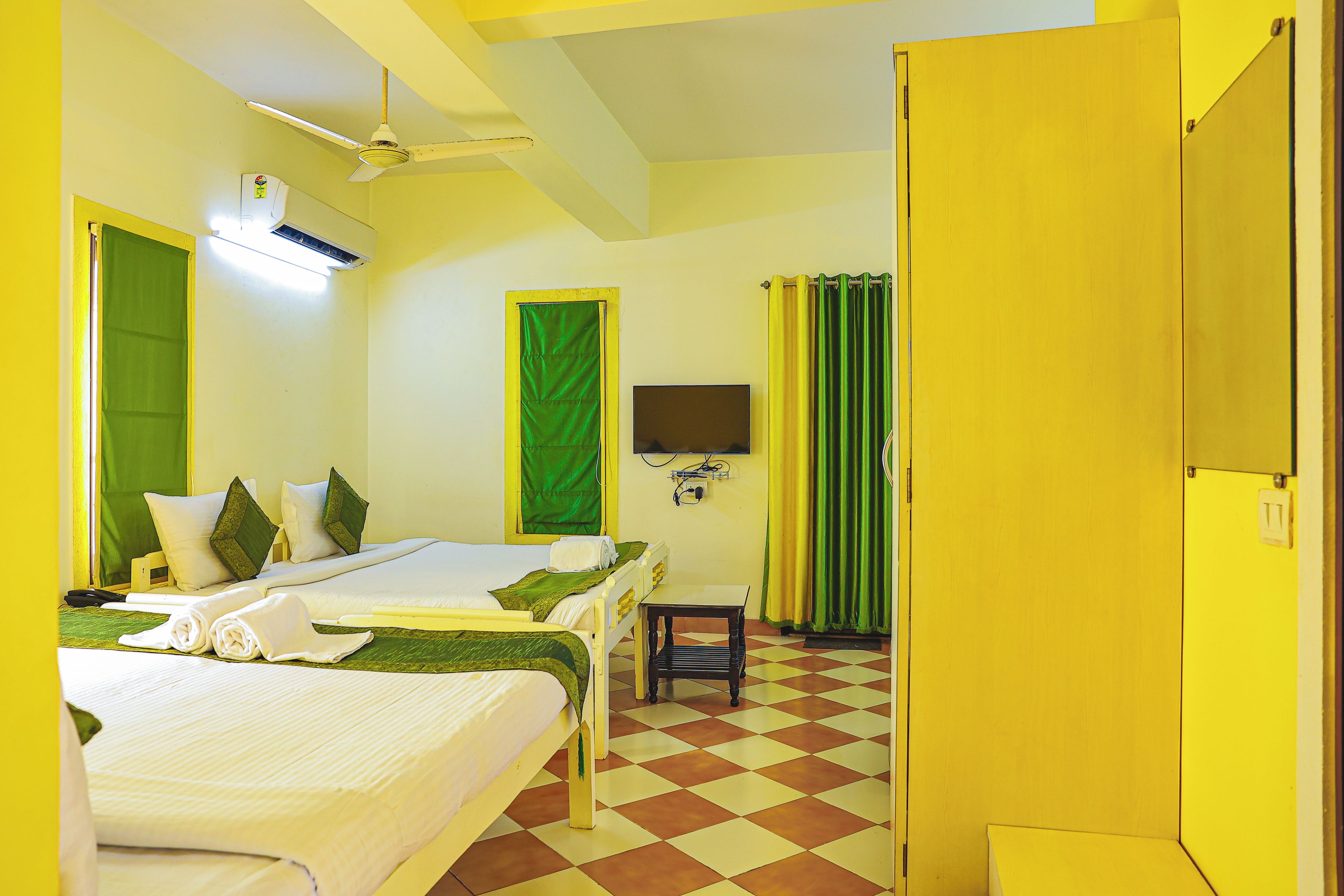 Une chambre d’hôtel avec deux lits, une télévision, un ventilateur de plafond et une fenêtre avec des rideaux.