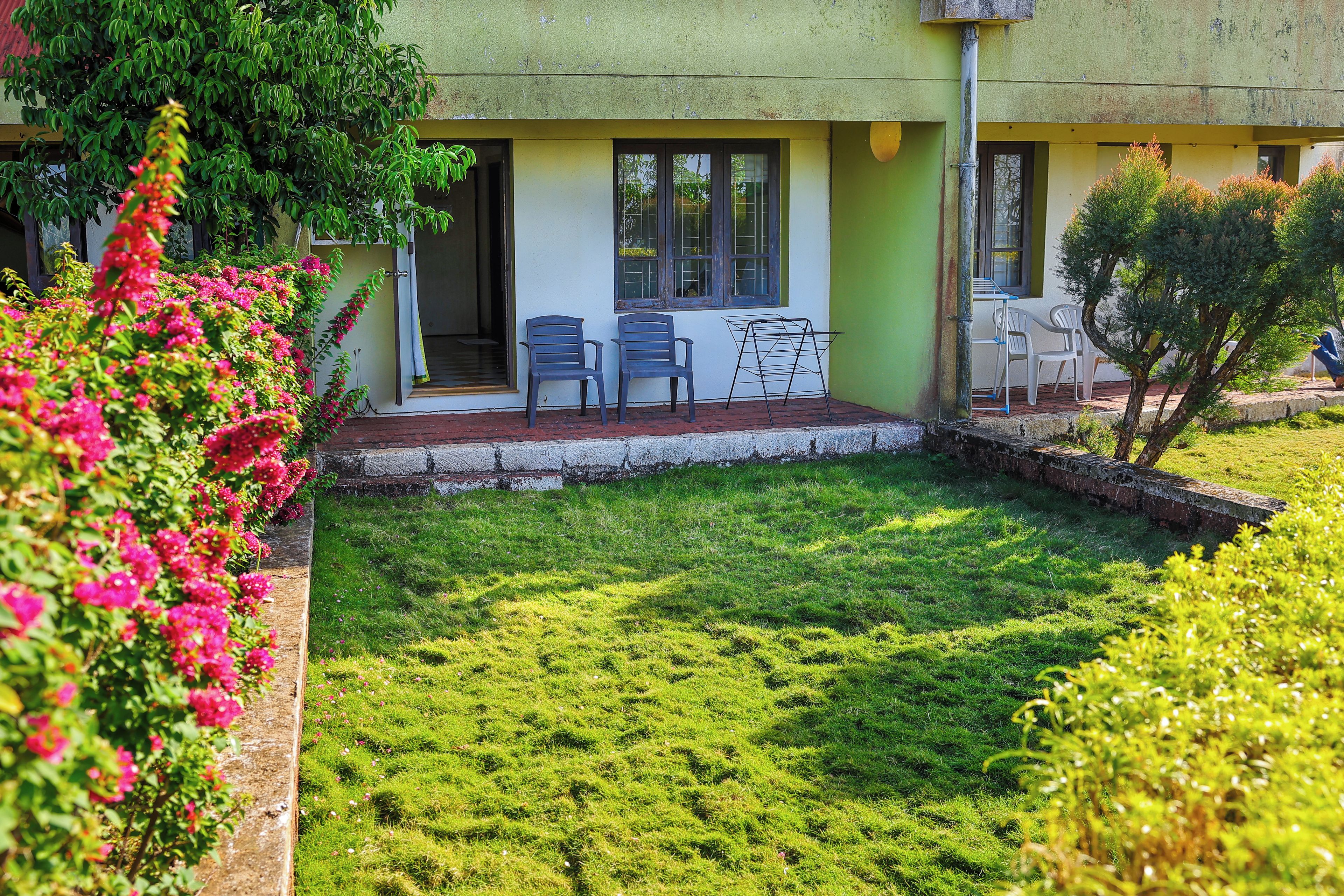 Un edificio con fachada verde, un pequeño patio con dos sillas y una zona ajardinada.