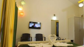 A hotel room with a bed, two chairs, a television, and a wardrobe. - Kokanwadi Resort (Ratnagiri)