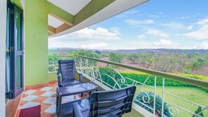 A balcony with two chairs and a table, overlooking a green landscape with trees and hills. - Kokanwadi Resort (Ratnagiri)