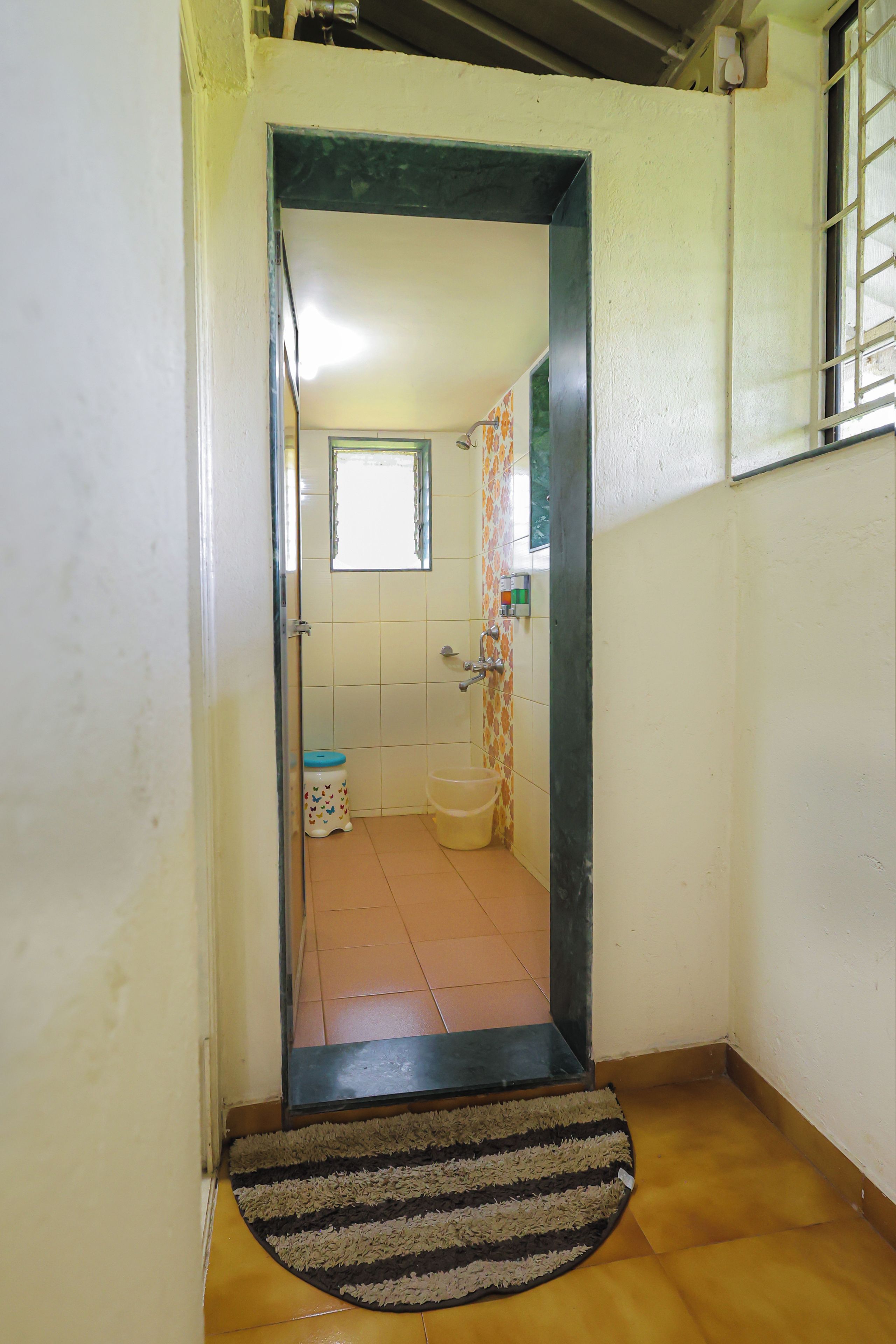 Un baño con ducha, inodoro y un taburete pequeño con un diseño colorido.
