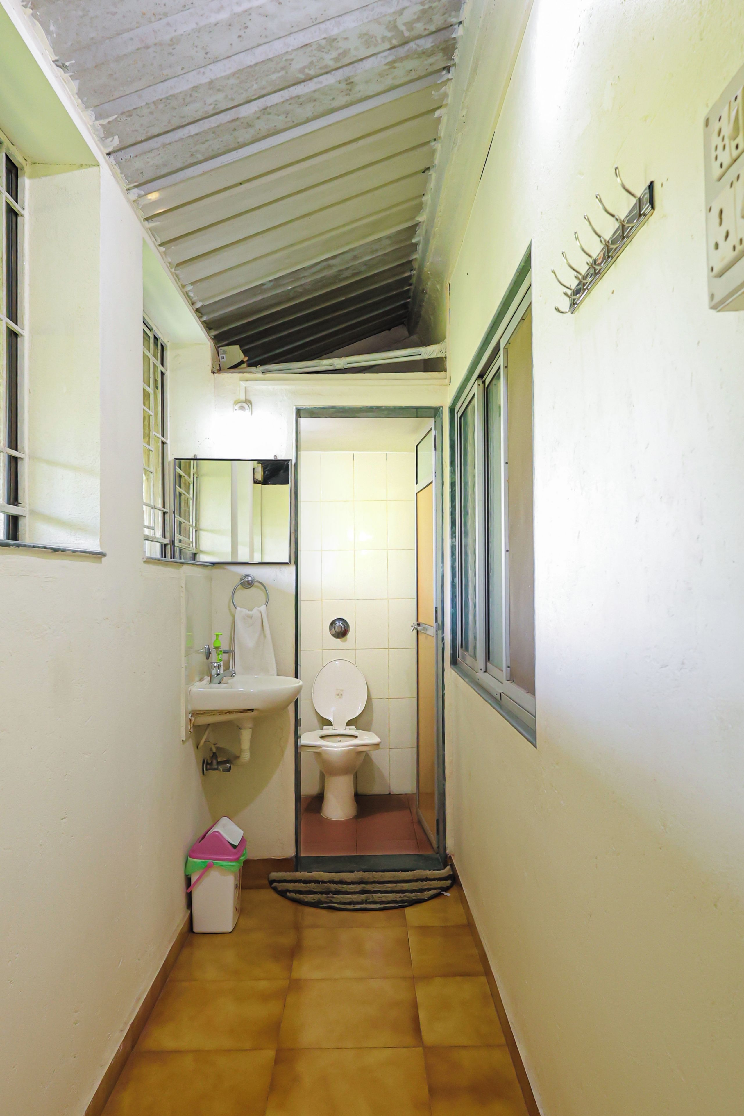 A narrow hallway with a toilet, sink, and a small trash bin.