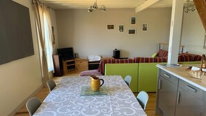 Een eetruimte met een tafel voor vier personen, een televisie en een bank op de achtergrond.