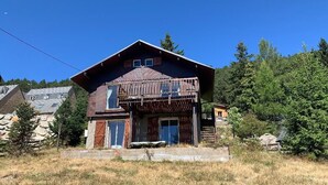 Een houten chalet met een ruim terras, een stenen fundering en een bebost achtergrond.