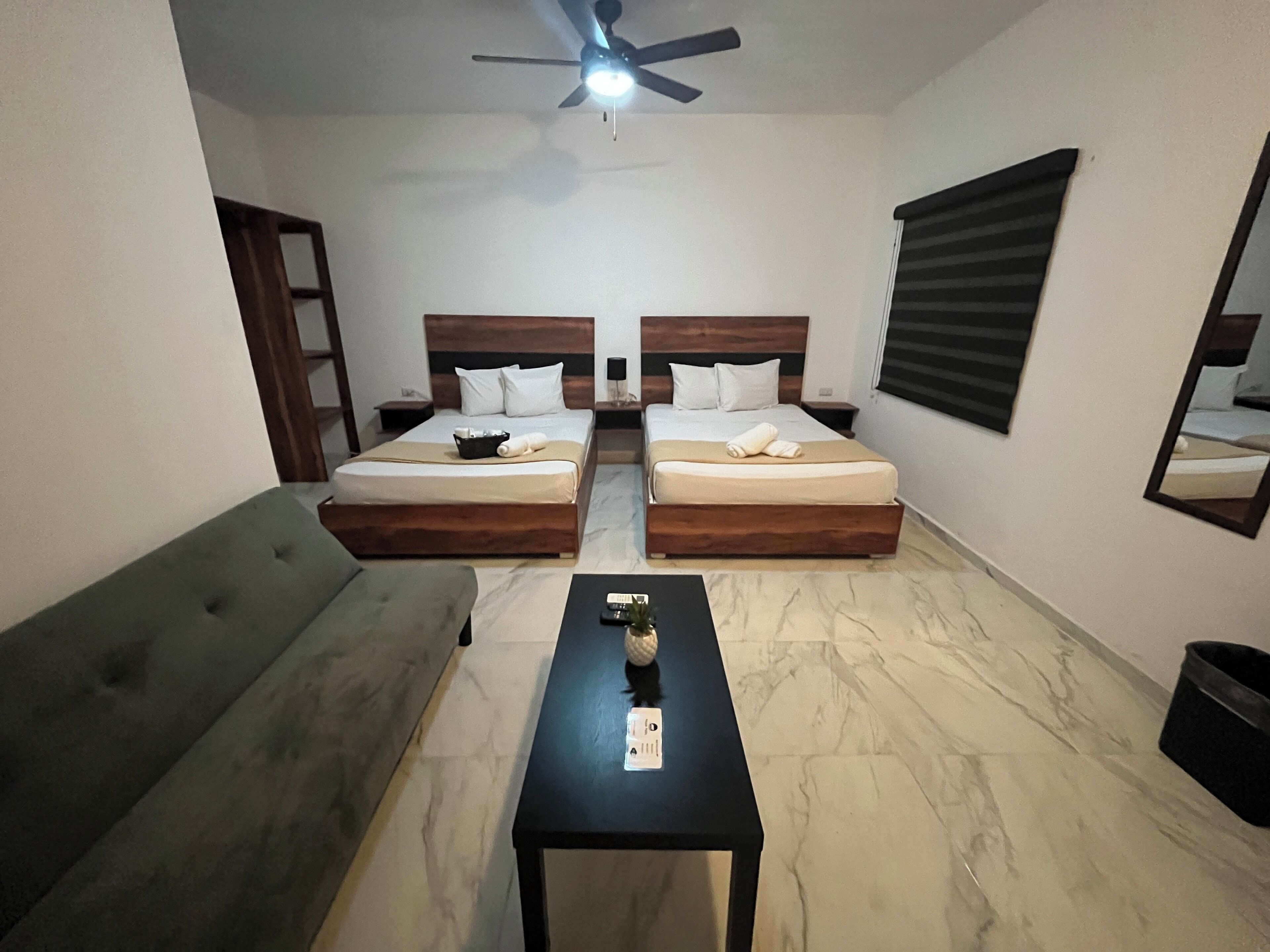 A hotel room with two beds, a sofa, a small table, and a ceiling fan.