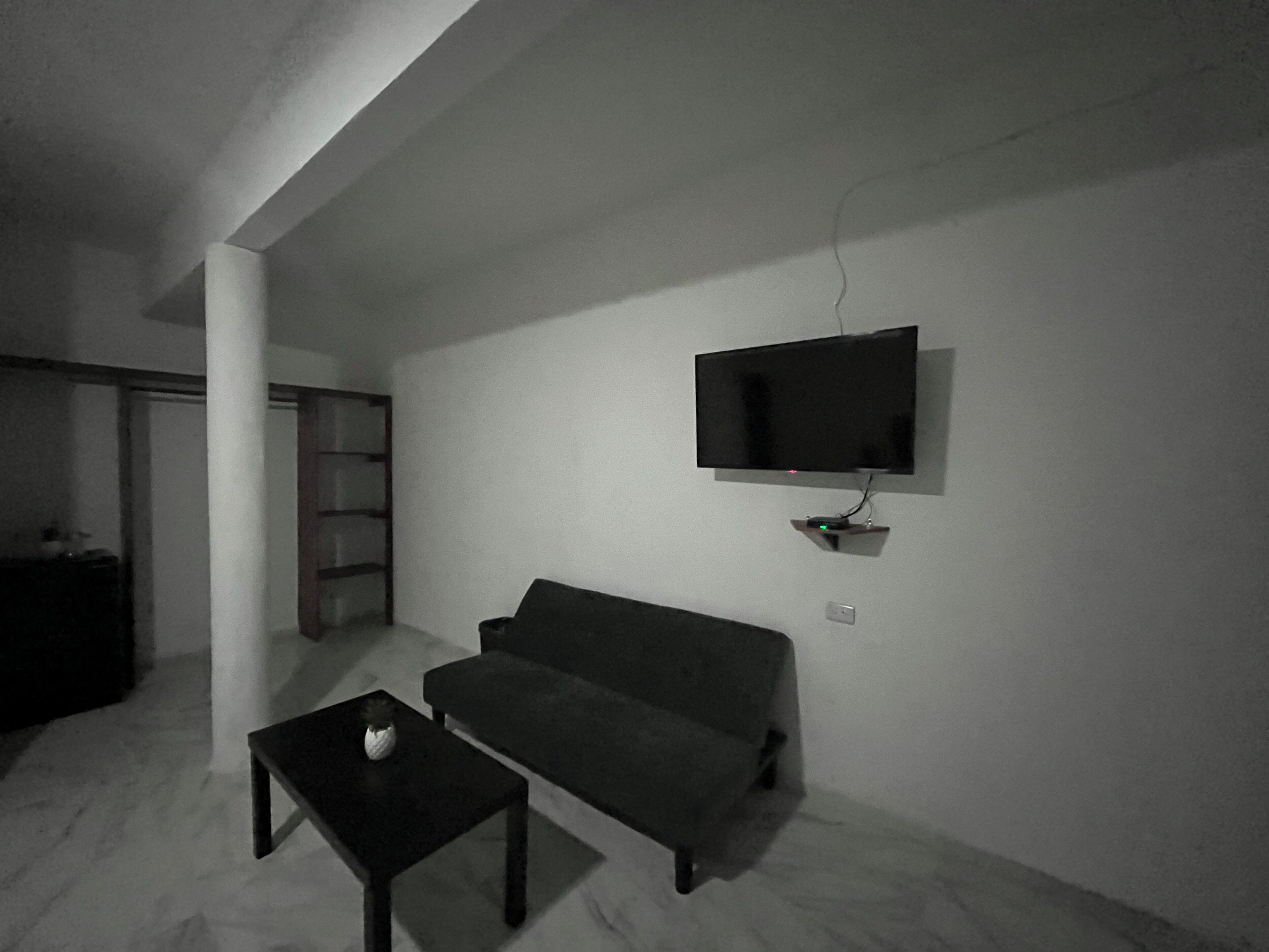 Un salon minimaliste avec un téléviseur à écran plat fixé au mur, un canapé de couleur sombre et une petite table basse.