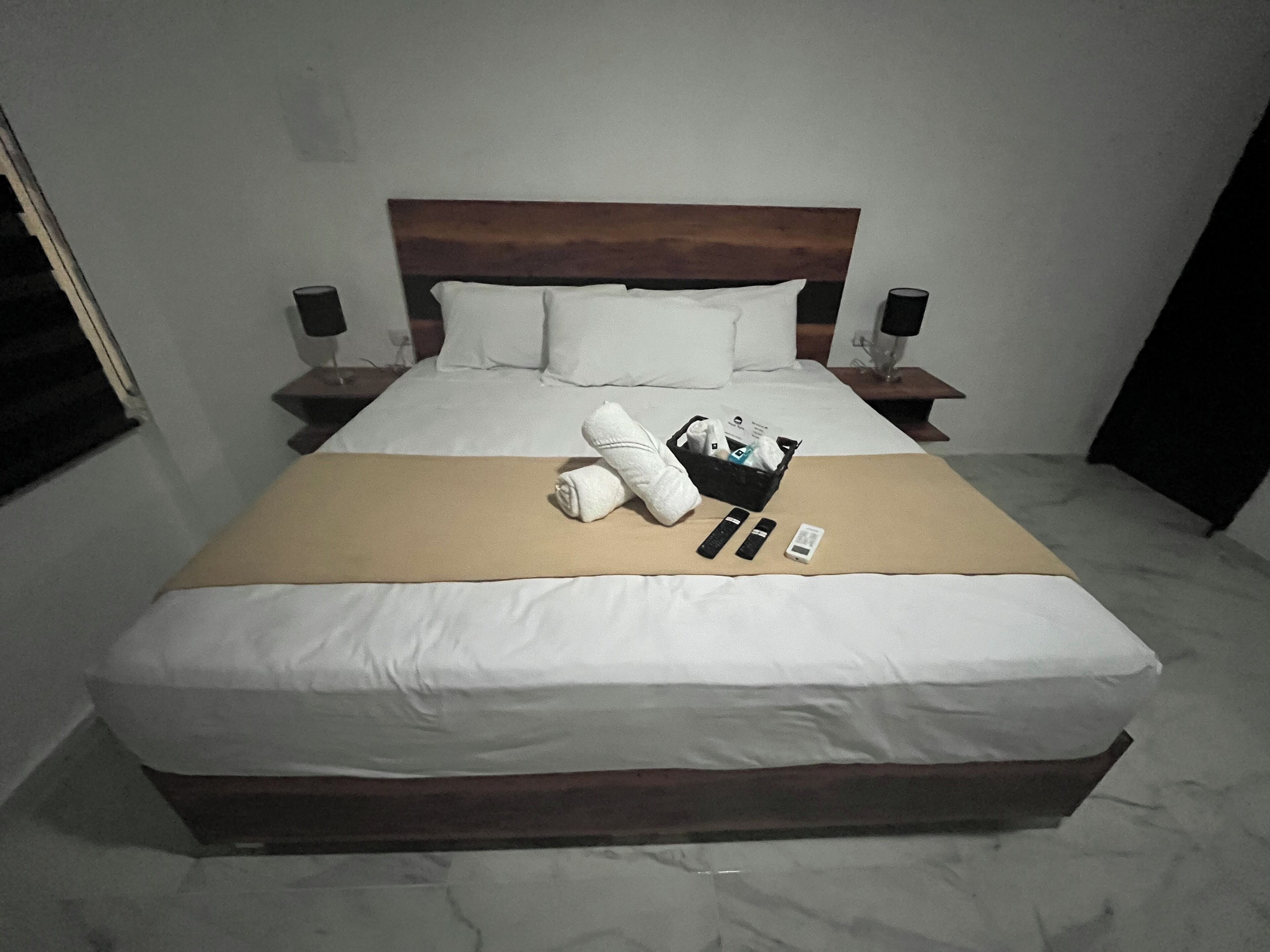 A neatly made bed with white linens, a brown blanket, and a set of toiletries including a towel, toothbrush, and a bottle.