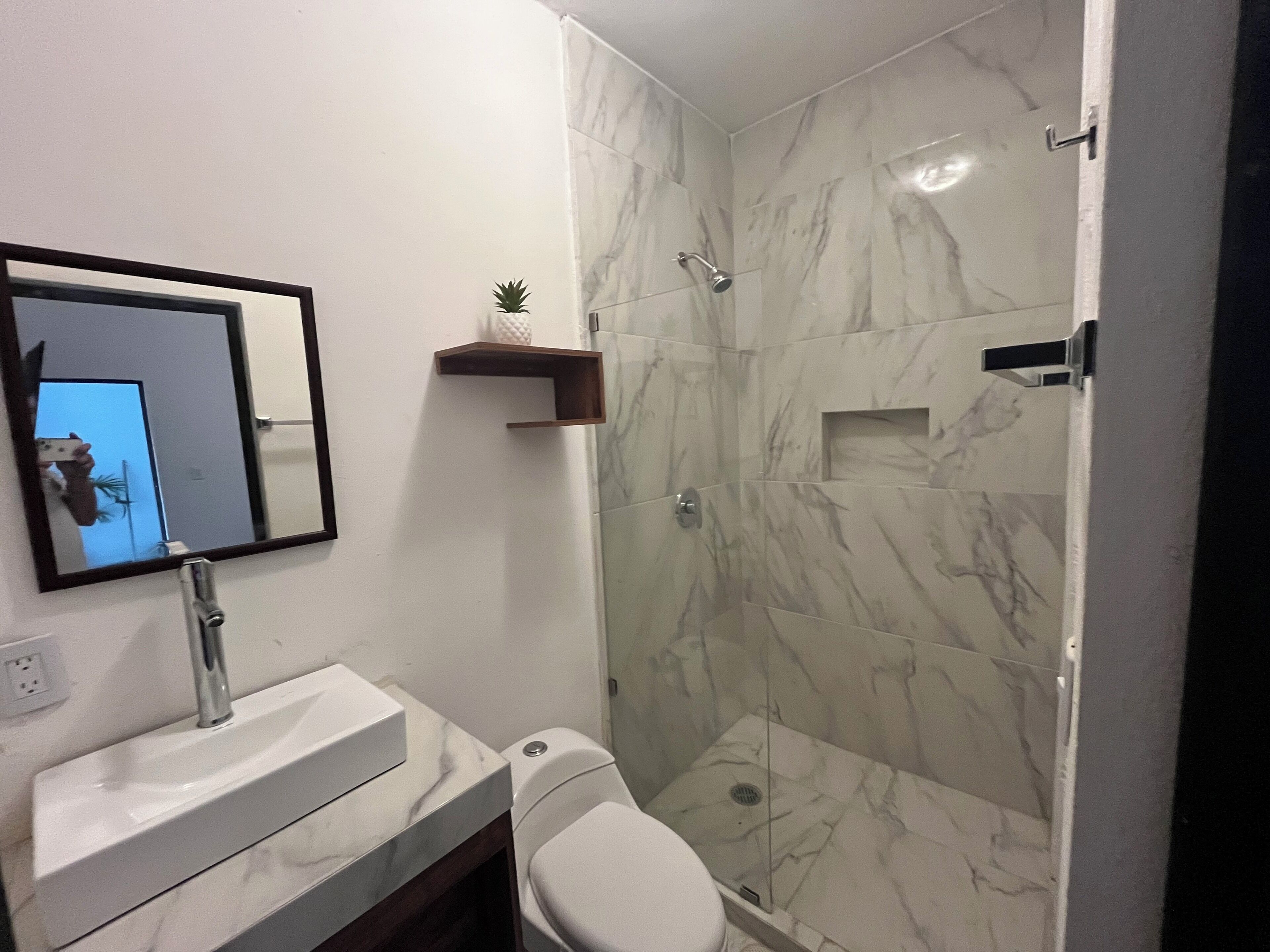 A bathroom with a marble shower, a sink with a mirror, and a toilet.