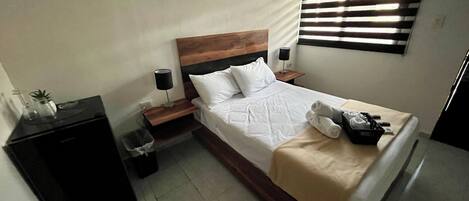 Une chambre d’hôtel équipée d’un lit, de tables de chevet, d’une poubelle et d’une fenêtre avec des stores.