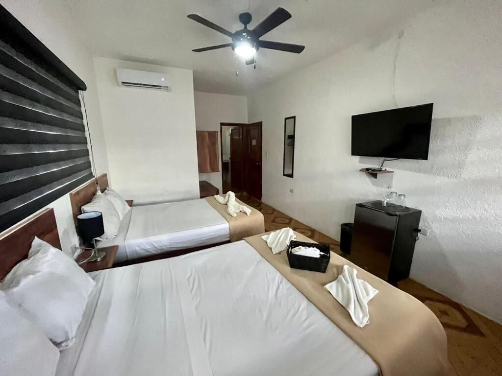 Une chambre d’hôtel avec deux lits, un ventilateur de plafond, un climatiseur, une télévision et un petit bureau avec une lampe.