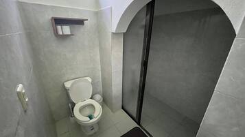 Un baño con inodoro, cabina de ducha y un estante pequeño sobre el inodoro.