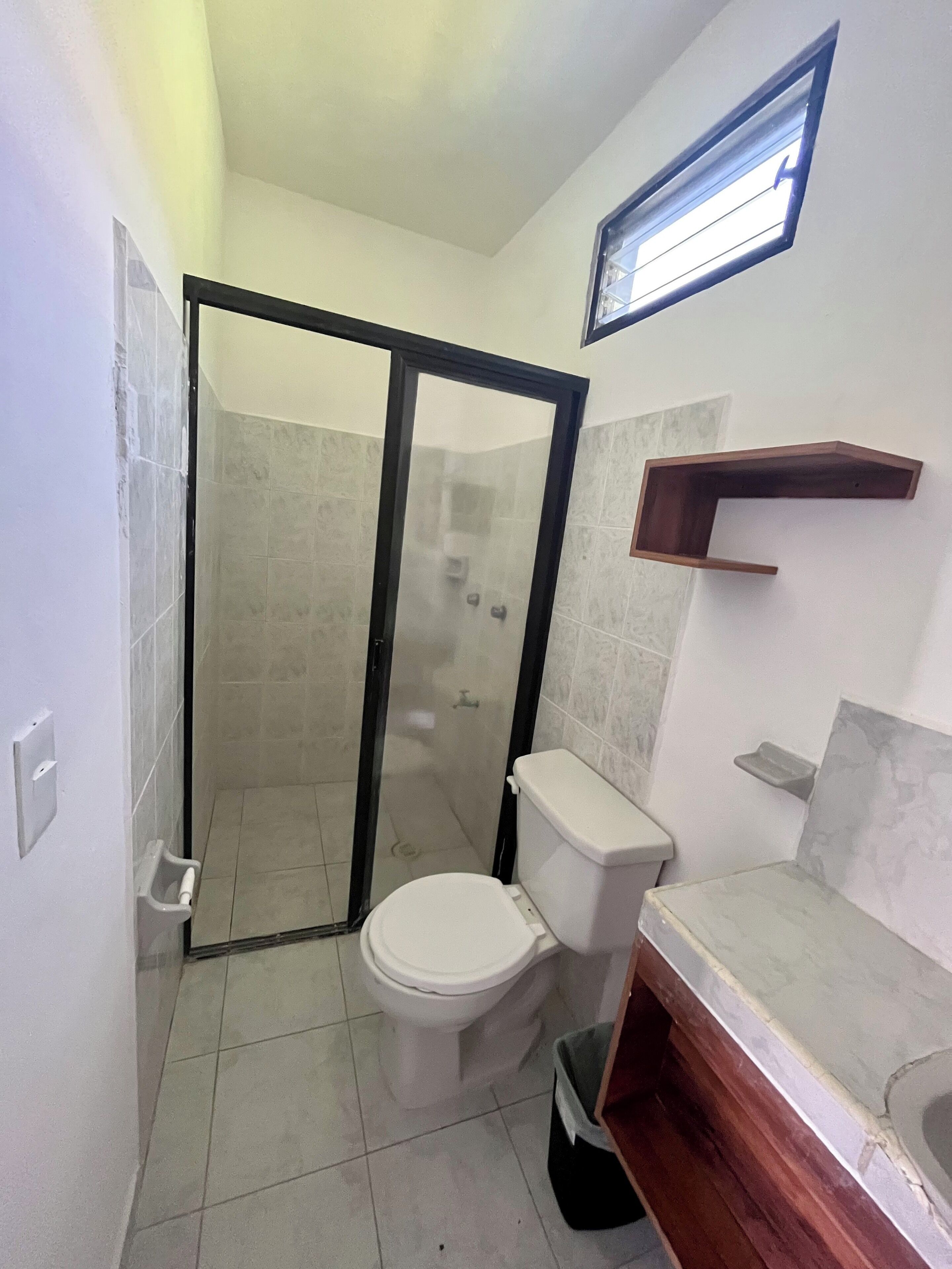 Ein Badezimmer mit Toilette, Duschkabine, Waschbecken und einer kleinen Ablagefläche.