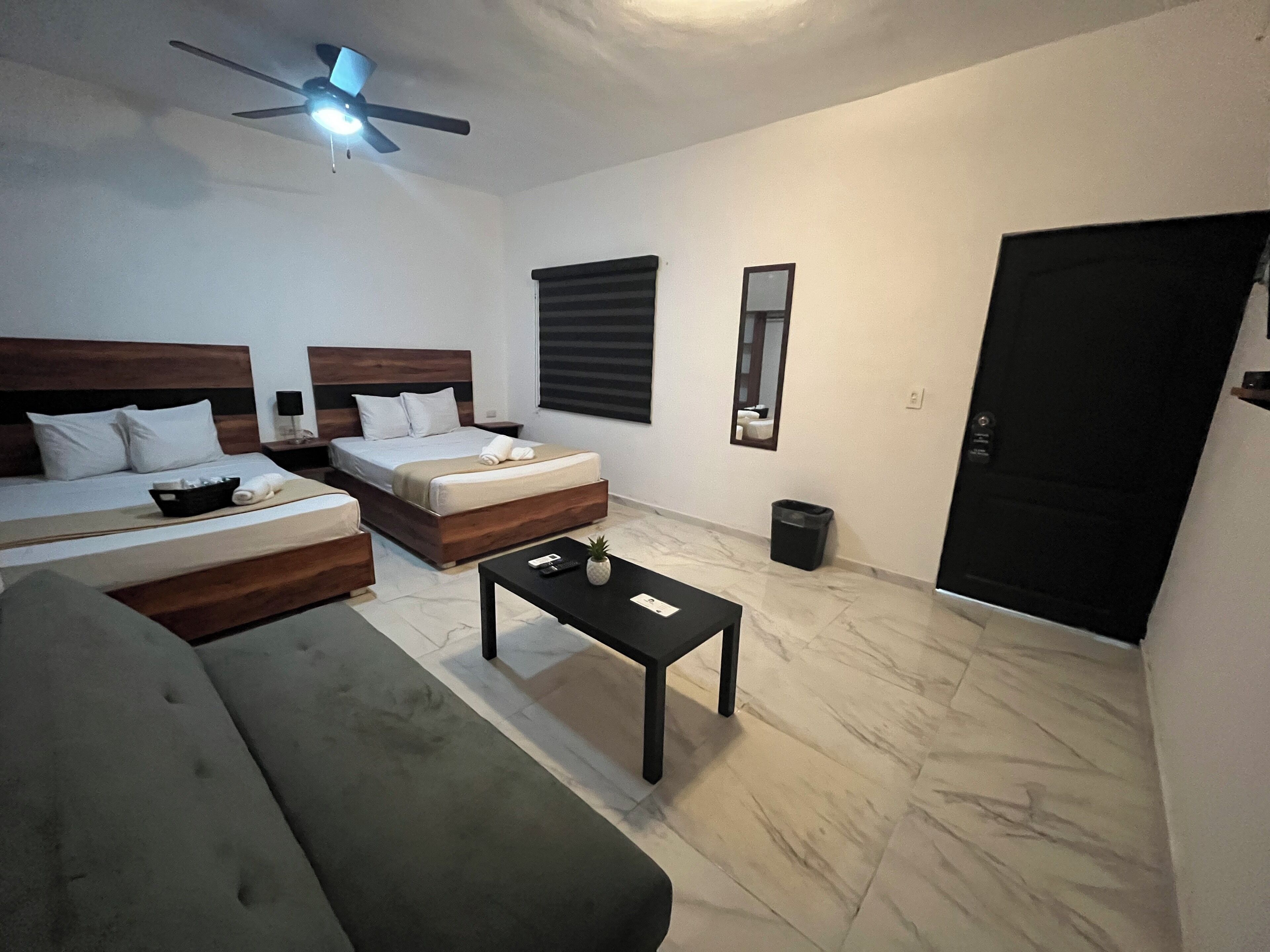 A modern hotel room with two beds, a sofa, a coffee table, and a ceiling fan.